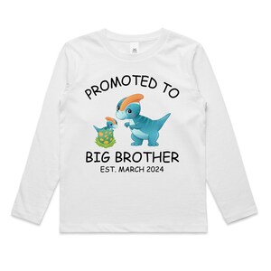 May include: White long-sleeved t-shirt featuring a blue and orange dinosaur graphic. The text "Promoted to Big Brother Est. March 2024" is printed on the shirt.