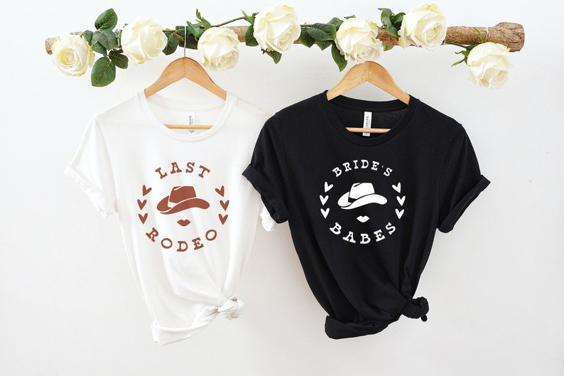 May include: Two white t-shirts with a brown cowboy hat graphic and the text "Last Rodeo" and "Bride's Babes" printed on them.