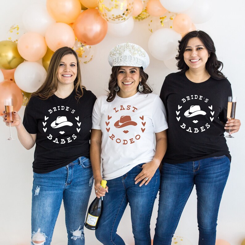 May include: Three friends wearing black and white t-shirts with a cowboy hat graphic and the text "Bride's Babes", "Last Rodeo", and "Bride's Babes".