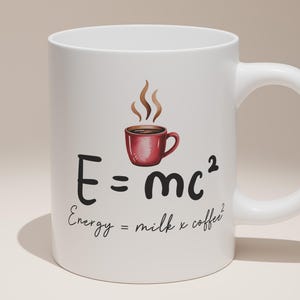 May include: White ceramic coffee mug featuring a red coffee cup illustration and the equation E=mc². The text below reads "Energy = milk x coffee²". The mug has a curved handle, ideal for hot drinks.