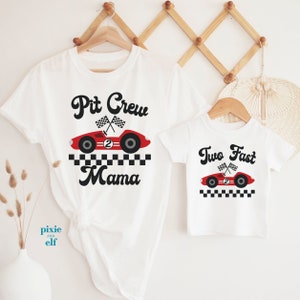 Peut inclure: Deux t-shirts blancs avec un motif de voiture de course rouge. Le plus grand t-shirt dit "Pit Crew Mama" et le plus petit dit "Two Fast".