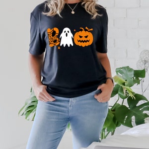 K&ouml;nnte beinhalten: Ein schwarzes T-Shirt mit einem Aufdruck eines Geistes, eines Spinnennetzes und eines K&uuml;rbisses mit dem Wort "BOO" in Orange und Schwarz.