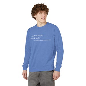 Puede incluir: Sudadera azul con cuello redondo y texto blanco: "michael eisner frank wells / humility is the final achievement /". La sudadera es de color liso y tiene mangas largas.
