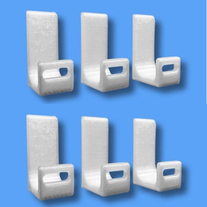 Könnte beinhalten: Sechs weiße Wandhaken aus Kunststoff mit J-Form. Die Haken sind so konzipiert, dass sie Gegenstände wie Mäntel, Hüte oder Taschen halten.