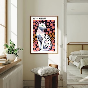 May include: A framed art print featuring a stylized cat with black polka dots, set against a black background with pink and orange floral patterns. The print includes the text "YAYOI KUSAMA" and "JAPANESE 1998".