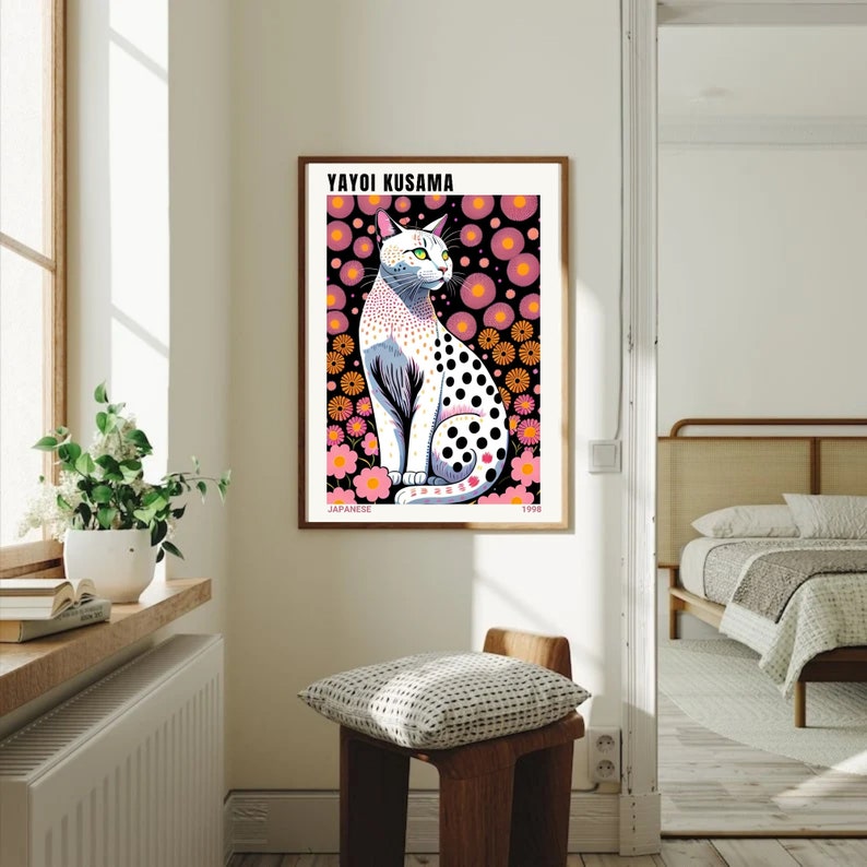 May include: A framed art print featuring a stylized cat with black polka dots, set against a black background with pink and orange floral patterns. The print includes the text "YAYOI KUSAMA" and "JAPANESE 1998".