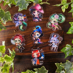 May include: Eight colorful cartoon character stickers with a variety of themes, including a mermaid, a witch, a fairy, and a goblin. The stickers are on a wooden surface with green ivy leaves around the edges.