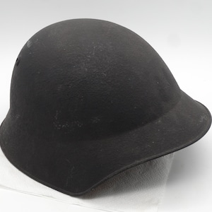May include: A black helmet with a peak, positioned on a white surface. The helmet has a curved form and a matte texture. The helmet appears to be constructed from a robust material.