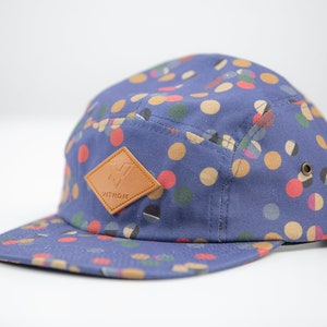 Op de afbeelding: Een blauwe en bruine baseballpet met een bruin leren patch waarop "WITHOM" staat.