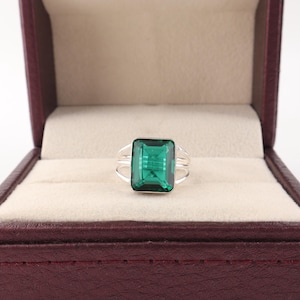 May include: A silver ring featuring a large, rectangular, emerald-green faceted gemstone set in a prong setting. The band of the ring is composed of three thin, parallel silver wires that converge at the base of the central stone setting.