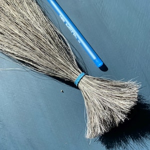 May include: A bundle of gray broom straw bound with a blue rubber band. A blue Bic Round Stic pen rests diagonally across the straw on a blue surface.
