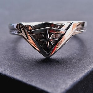 Pu&ograve; includere: Un anello d'argento con un design a stella stilizzato all'interno di una forma a scudo.