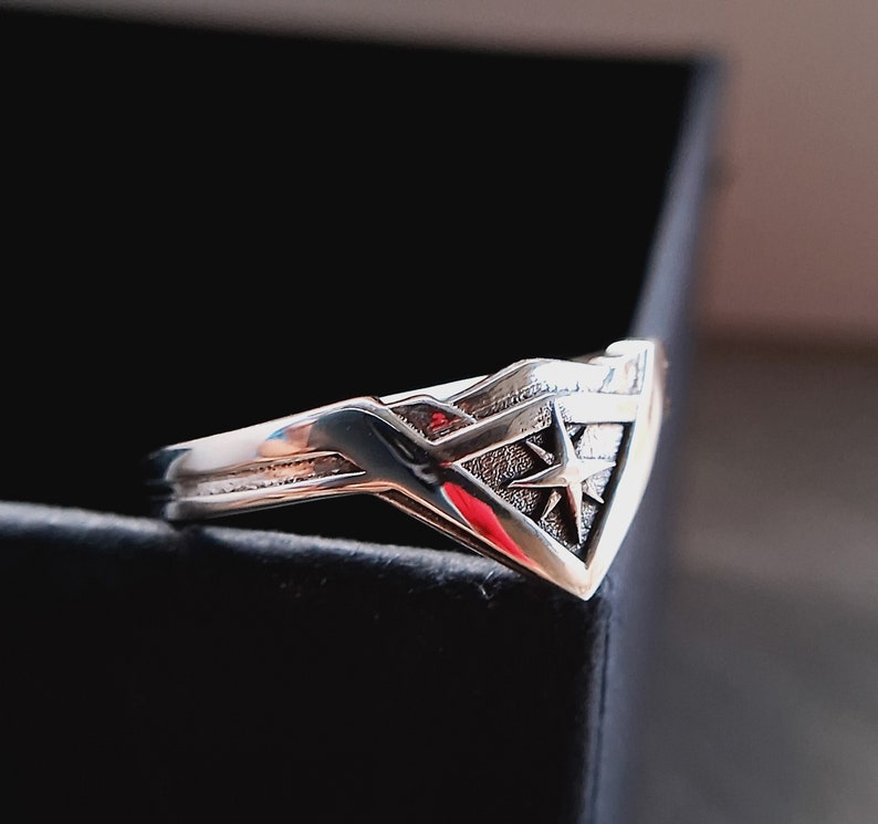 Pu&ograve; includere: Un anello d'argento con un design a stella stilizzato. L'anello ha la forma di un triangolo con una punta appuntita.