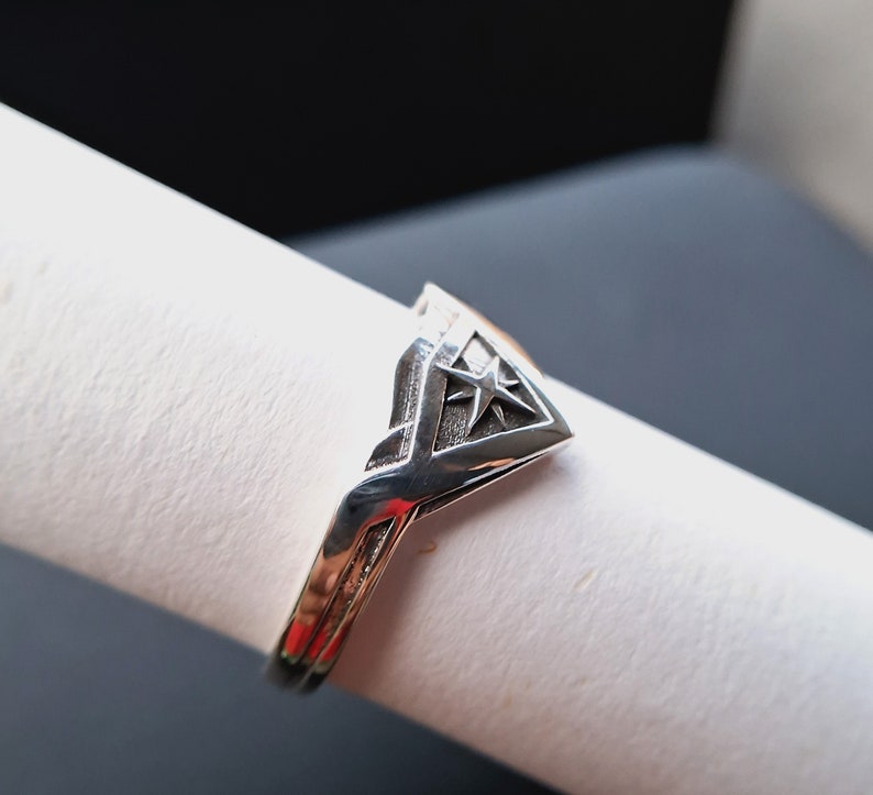 Pu&ograve; includere: Un anello d'argento con un design triangolare che presenta una stella al centro.
