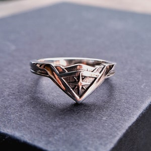 Pu&ograve; includere: Un anello d'argento con un design a stella stilizzato all'interno di una forma triangolare.