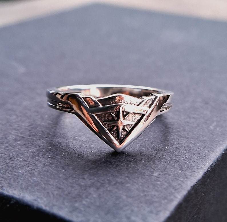 Pu&ograve; includere: Un anello d'argento con un design a stella stilizzato all'interno di una forma triangolare.