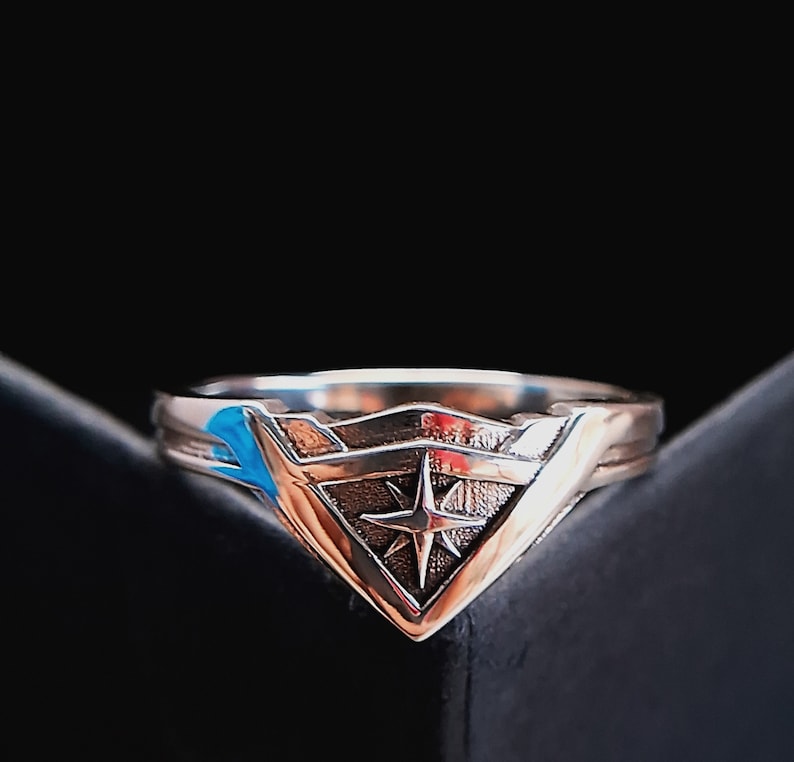 Pu&ograve; includere: Un anello d'argento con un design a stella stilizzato al centro. L'anello ha la forma di un triangolo con una punta.
