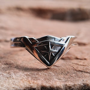 Pu&ograve; includere: Un anello d'argento con un design a stella stilizzato al centro. L'anello ha la forma di uno scudo con la parte inferiore a punta.