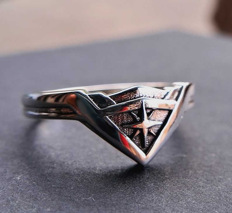 Pu&ograve; includere: Un anello d'argento con un design a logo di Wonder Woman. Il logo &egrave; una 'W' stilizzata con una stella al centro.