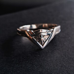 Pu&ograve; includere: Un anello d'argento con un design a stella stilizzato al centro di una forma triangolare.
