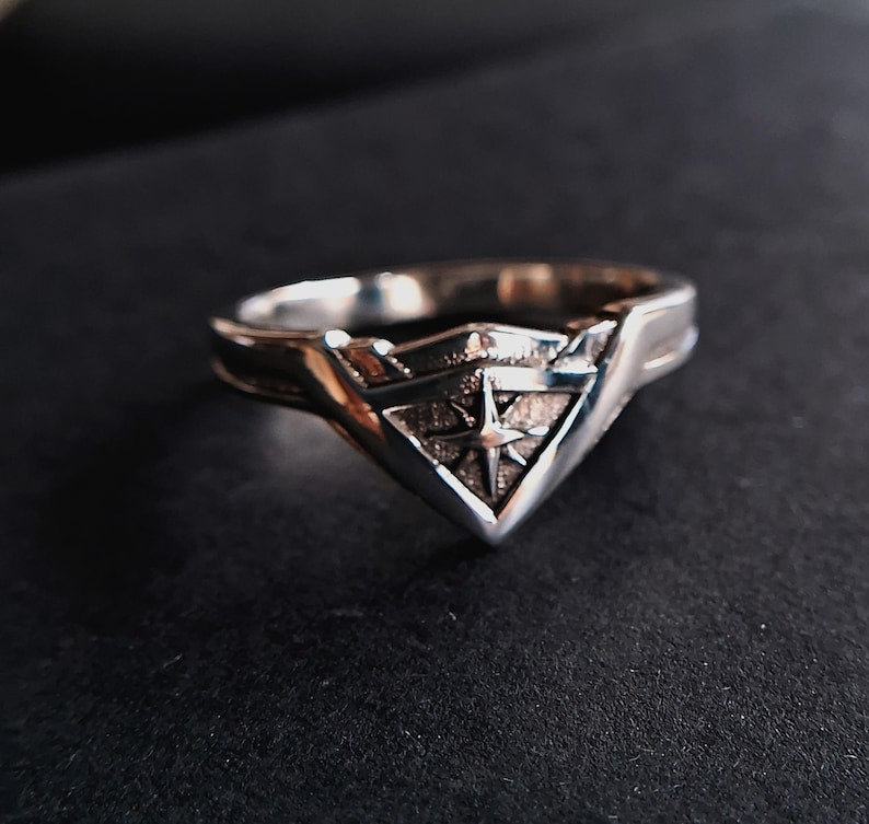 Pu&ograve; includere: Un anello d'argento con un design a stella stilizzato al centro di una forma triangolare.