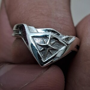 Pu&ograve; includere: Un anello d'argento con un design a forma di stella all'interno di un triangolo. L'anello &egrave; realizzato in metallo lucido e ha una finitura liscia.