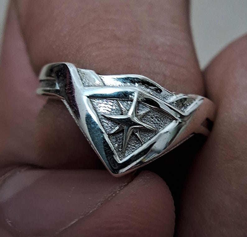 Pu&ograve; includere: Un anello d'argento con un design a forma di stella all'interno di un triangolo. L'anello &egrave; realizzato in metallo lucido e ha una finitura liscia.