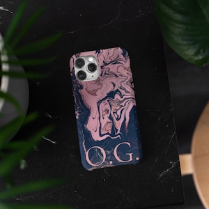 以下が含まれることがあります： ピンクとブラックのマーブル模様のスマホケースで、ゴールドの文字で「O.G.」のイニシャルが入っています。