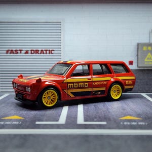 May include: A red and yellow toy car with "MOMO" and "KAIDOHouse" printed on the side. The car is a station wagon with black accents and yellow wheels.
