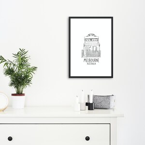 May include: Black and white line drawing of a house with the text "MELBOURNE AUSTRALIA" underneath. The drawing is framed in a black frame and hanging on a white wall.