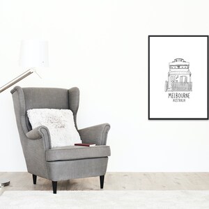 May include: Black and white line drawing of a house with the text "MELBOURNE AUSTRALIA" underneath. The drawing is framed and hanging on a white wall above a gray armchair.