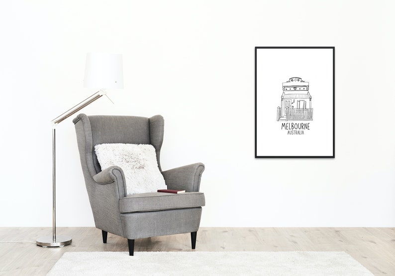 May include: Black and white line drawing of a house with the text "MELBOURNE AUSTRALIA" underneath. The drawing is framed and hanging on a white wall above a gray armchair.