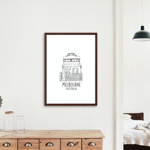 May include: Black and white line drawing of a house with the text "MELBOURNE AUSTRALIA" underneath. The drawing is framed in a brown frame and is hanging on a white wall.