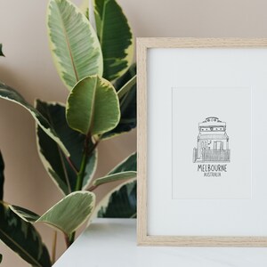 May include: A framed black and white line drawing of a house with the text "MELBOURNE AUSTRALIA" underneath. The frame is light wood and the drawing is on white paper.