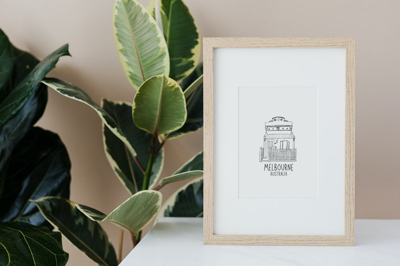 May include: A framed black and white line drawing of a house with the text "MELBOURNE AUSTRALIA" underneath. The frame is light wood and the drawing is on white paper.