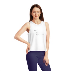 Pode incluir: Top branco com a frase "drinks on me" em escrita preta. O top é sem mangas e tem decote redondo. A modelo está vestindo leggings azul marinho.