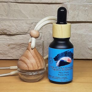 May include: A fragrance oil refill bottle with a black dropper cap and a blue label featuring a graphic of a colourful umbrella. The label text reads Huile de parfum Recharge, Fragrance Oil Refill, Musc Frais, Fresh musk. Beside it is a glass diffuser.