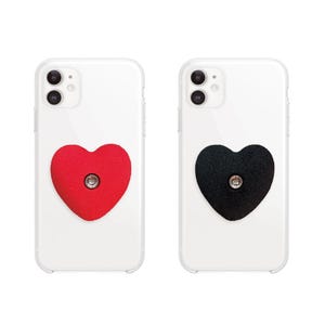 May include: Two clear phone cases each feature a heart-shaped phone grip. One grip is red, the other is black. Each grip has a silver-colored button in the center. The phones are white and have a dual-lens camera.