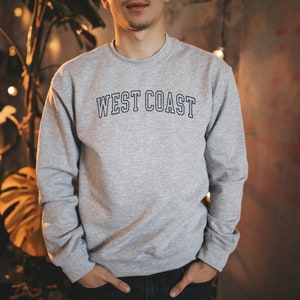 May include: A gray sweatshirt with the text "WEST COAST" in blue outlined letters.