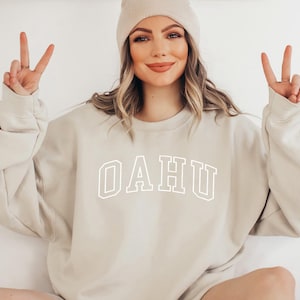 May include: A beige sweatshirt with the word "OAHU" printed in white on the front. The sweatshirt has a crew neck and long sleeves.