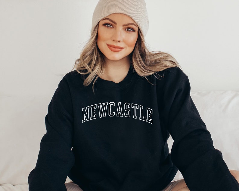 May include: A black sweatshirt with the word "NEWCASTLE" printed in white on the front. The sweatshirt has a crew neck and long sleeves.