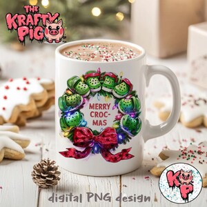Könnte beinhalten: Weiße Kaffeetasse mit einem grünen, roten und weißen Weihnachtskranz-Design mit dem Text "Merry Croc-Mas".