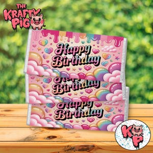 May include: Three stacked candy bar wrappers with a pink background and the words "Happy Birthday" in a retro font. The wrappers feature colorful hearts, stars, and rainbow-colored orbs. The top left corner has a logo with a pig.