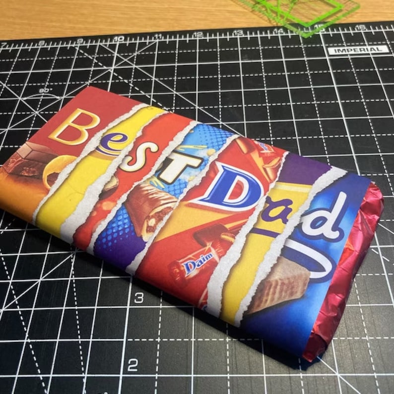 Pode incluir: Uma barra de chocolate embrulhada em papel alum&iacute;nio colorido com as palavras "Best Dad" impressas nela. O papel alum&iacute;nio est&aacute; rasgado em alguns lugares para revelar as barras de chocolate que est&atilde;o por baixo.