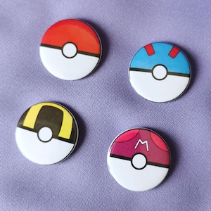 Può includere: Quattro spille rotonde e colorate di Poké Ball di Pokémon. Le spille presentano una Poké Ball rossa, blu, gialla e rosa con un centro bianco e un contorno nero.