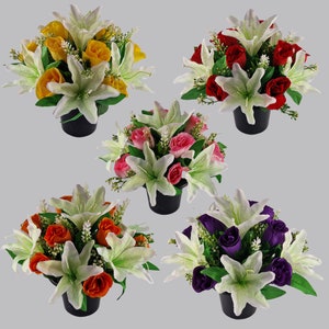 May include: Artificial flower arrangements in black pots. Each pot features white lilies and roses in yellow, red, pink, orange, and purple. Green foliage and small white flowers are also present, creating a vibrant display.