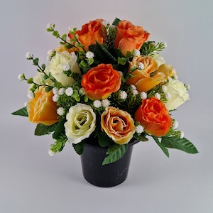 May include: A bouquet of artificial flowers in a black pot. The flowers are a mix of orange, yellow, and white roses with small white flowers.