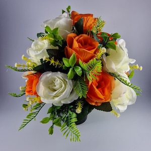 May include: A bouquet of artificial flowers in a white and orange colour scheme. The bouquet features white roses, orange roses, and green foliage.