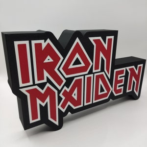 Op de afbeelding: Zwarte en rode 3D-wanddecoratie met de tekst "IRON MAIDEN" in een vet, gestileerd lettertype.