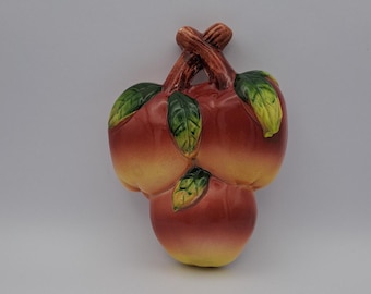May include: Ceramic wall decor featuring three red and yellow apples with green leaves. The apples are arranged in a cluster and have a realistic appearance.